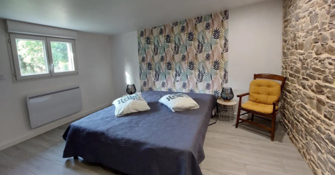 chambre avec tête de lit en papier peint de feuilles colorées, lit double avec couverture bleue et chaise en bois et assise jaune