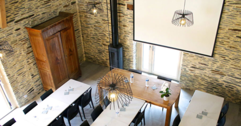 salle à manger aux murs en pierre, poêle à bois noir et suspensions contemporaines métalliques noires vue du dessus