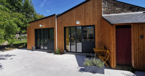 maison de plein pied avec bardage de bois, deux portes fenêtres contemporaines aux huisseries noires et terrasse effet béton gris clair