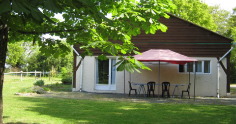 petite maison de plein pied avec bardage de bois sur le pignon, jardin arboré, terrasse et tonnelle rouge