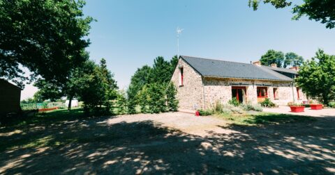 longère en pierre avec huisseries et jardinières rouges sur un terrain ombragé