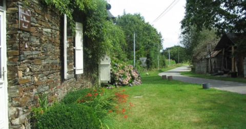longère en pierre aux volets en bois blanc donnant sur un petit jardin fleuri en bord de route communale
