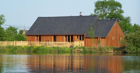 maison de plein pied avec bardage de bois, toit en ardoise, barrière en bois donnant sur un étang