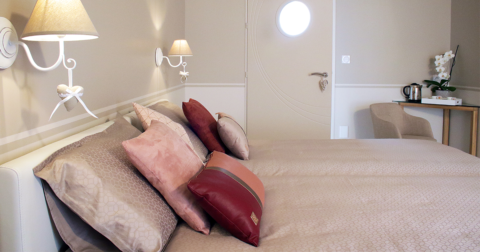 chambre moderne avec murs blanc et beige, lit avec parure dans les mêmes tons et table d'angle en bois et fauteuil beige