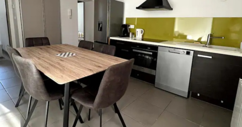 salle à manger avec table en bois et 6 fauteuils en velours gris dans une cuisine aménagée noire et blanche et crédence verte