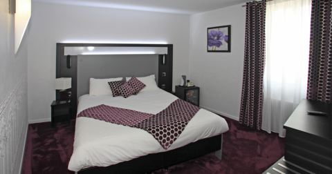 chambre dans les tons blancs et violet avec lit double, grande tête de lit, rideaux et moquette