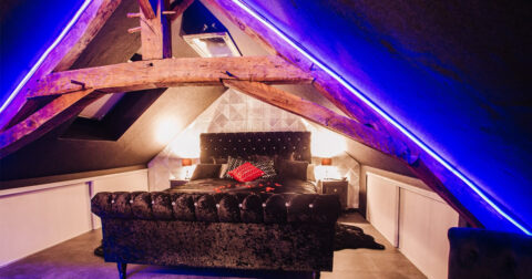 chambre cosy sous toit mansardé de poutres anciennes, lit velours noir et lumière tamisée