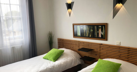 chambre aux murs blancs, tête de lit en bois, deux lits simples avec coussins verts