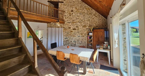 salle à manger avec mur en pierre apparente, baie vitrée, escalier et rambarde en bois