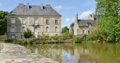 maison de maître en pierre avec huisseries blanches au bord d'un étang avec muret en pierre