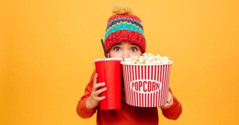 petite fille avec bonnet d'hiver qui se cache derrière son soda et son pop corn