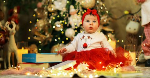 Petite fille de 1 ans en tenue de Noël assise par terre entourée de livres