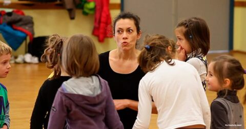 jeune femme accroupie discutant avec des enfants dans une salle de danse