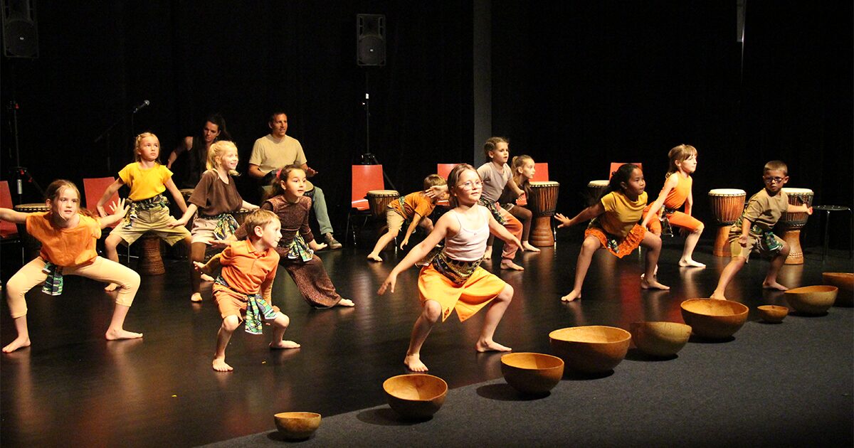 groupe d'enfants sur scène dansant au milieu de tambourins posés au sol