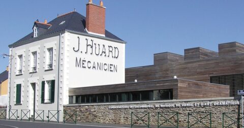 Façade blanche d'une grande maison de ville avec l'inscription "J Huard mécanicien"