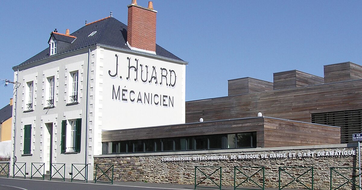 Façade blanche d'une grande maison de ville avec l'inscription "J Huard mécanicien"