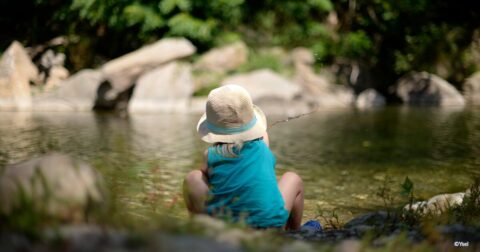 photographie d'une fillette de dos avec un chapeau assise au bord d'une rivière