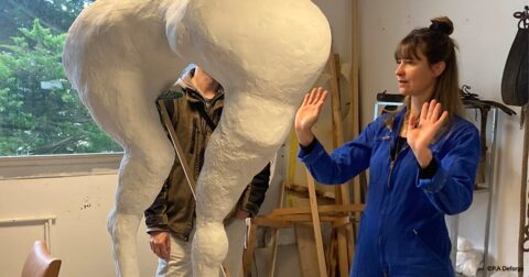 femme en bleu de travail dans son atelier discutant de sa sculpture avec une autre personne