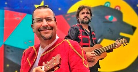 un chanteur en costume rouge et un guitariste devant une fresque avec un loup coloré