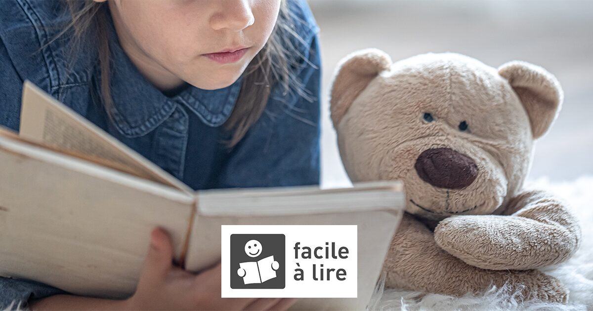 petite fille et un ours en peluche lisant un livre allongé sur un tapis