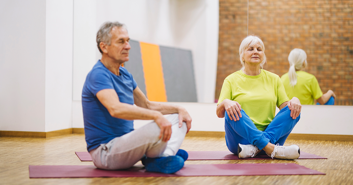 deux retraités homme et femme en position de yoga sur des tapis dans une salle