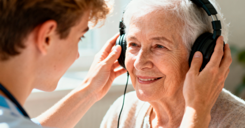 Retraitée assistée d'un personne lui posant un casque audio sur la tête
