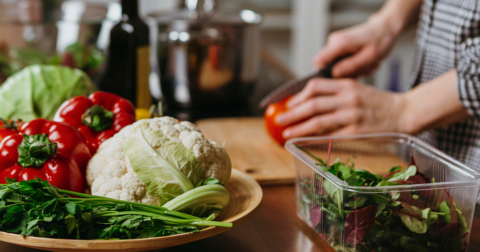 légumes sur un plan de travail et une personne coupe un poivron rouge