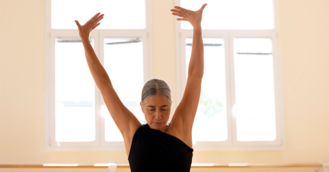 femme sénior dans une salle de danse la tête baissée et les bras en l'air
