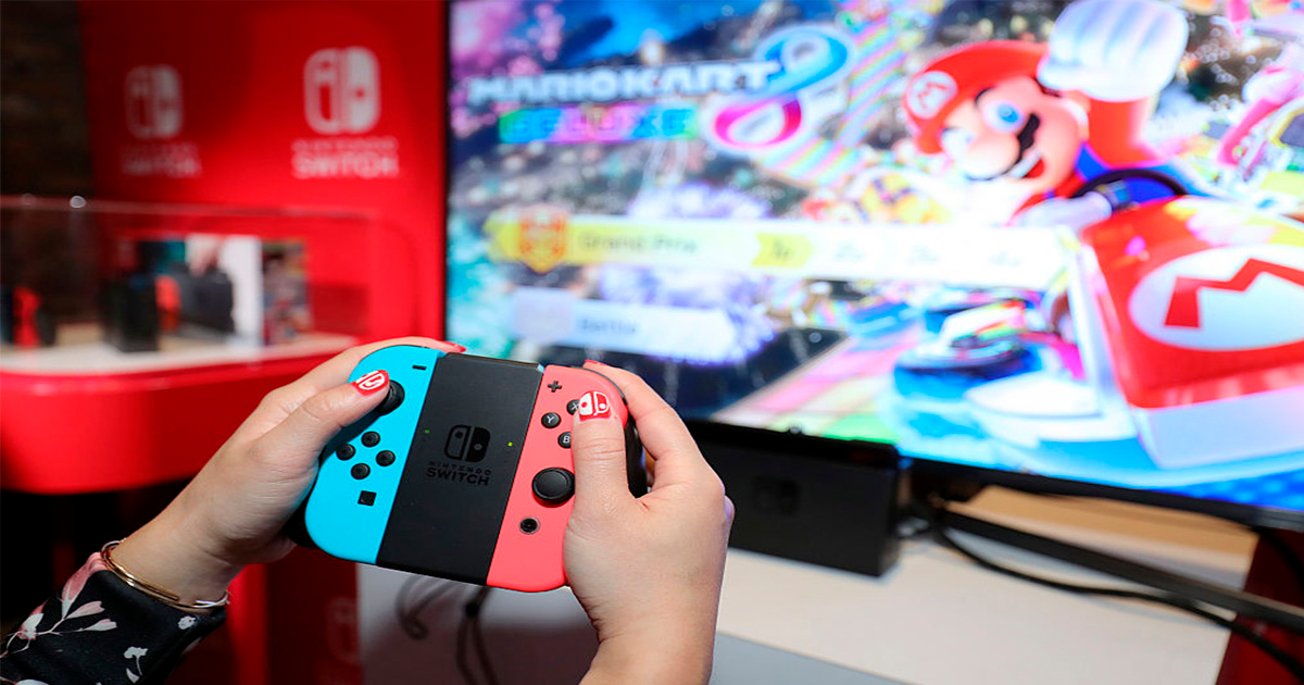 mains tenant une manette devant un écran de jeu vidéo Mario Kart
